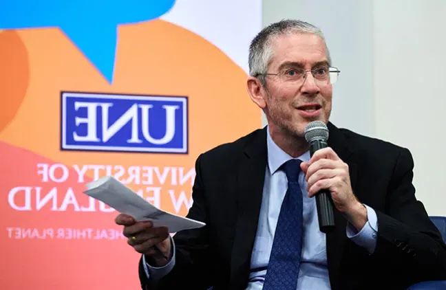 Bryan Caplan holding the microphone and notes in another hand while responding to a question posed by Shannon Zlotkowski